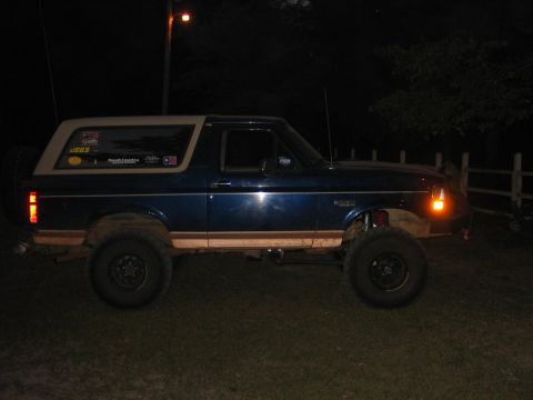 1995 Ford Bronco - A lifted blue Ford Bronco with a tan top is parked on grass at night.