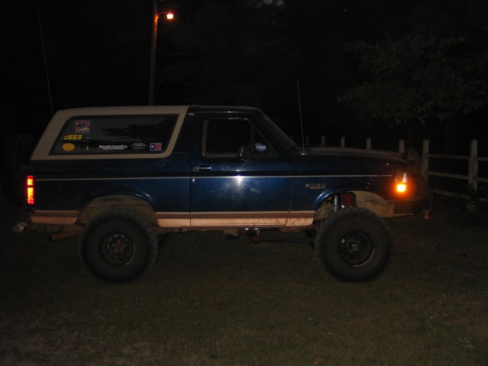 Lifted dark blue and tan Ford Bronco with off-road tires parked on grass at night