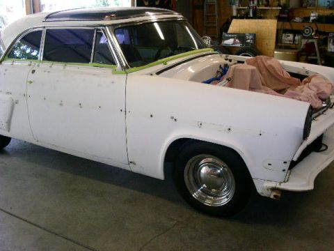 1954 Ford Crestline - A white coupe is in a garage, with its hood open and covered engine components, appearing to be in the middle of a restoration project.