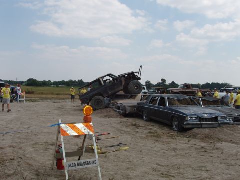 2000 Chevrolet Tahoe - An off-road vehicle is precariously balanced on top of several crushed sedans in a sandy lot.