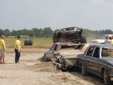 2000 Chevrolet Tahoe - A Jeep is positioned on top of several wrecked cars during an event, with spectators watching in the background.