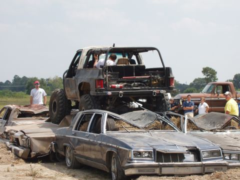 2000 Chevrolet Tahoe - A lifted truck is positioned on top of several destroyed sedans, with spectators observing the scene.