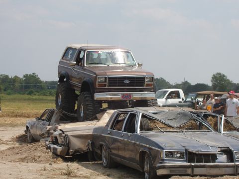 2000 Chevrolet Tahoe - A lifted brown Ford Bronco is positioned on top of several crushed sedans at an outdoor event.