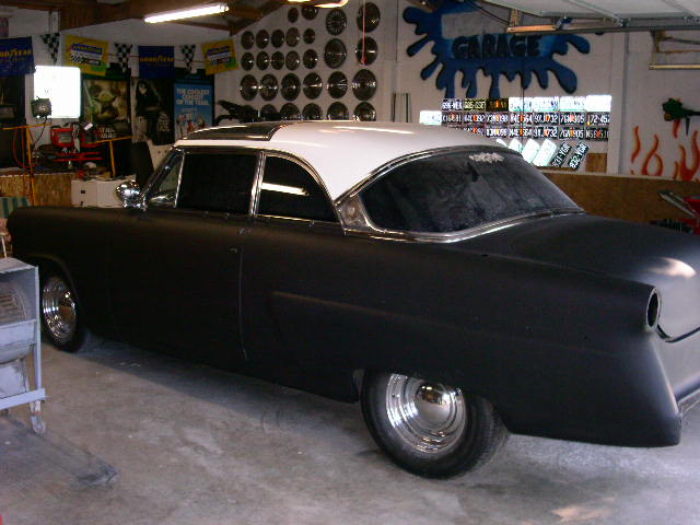 1950s Ford sedan in black primer with white roof parked in a decorated garage