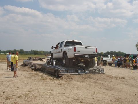 2000 Chevrolet Tahoe - A large white pickup truck is positioned on top of a pile of cars in a dirt lot.