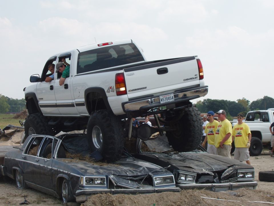 White 2000 Chevrolet Tahoe with large tires crushing two sedans, people watching