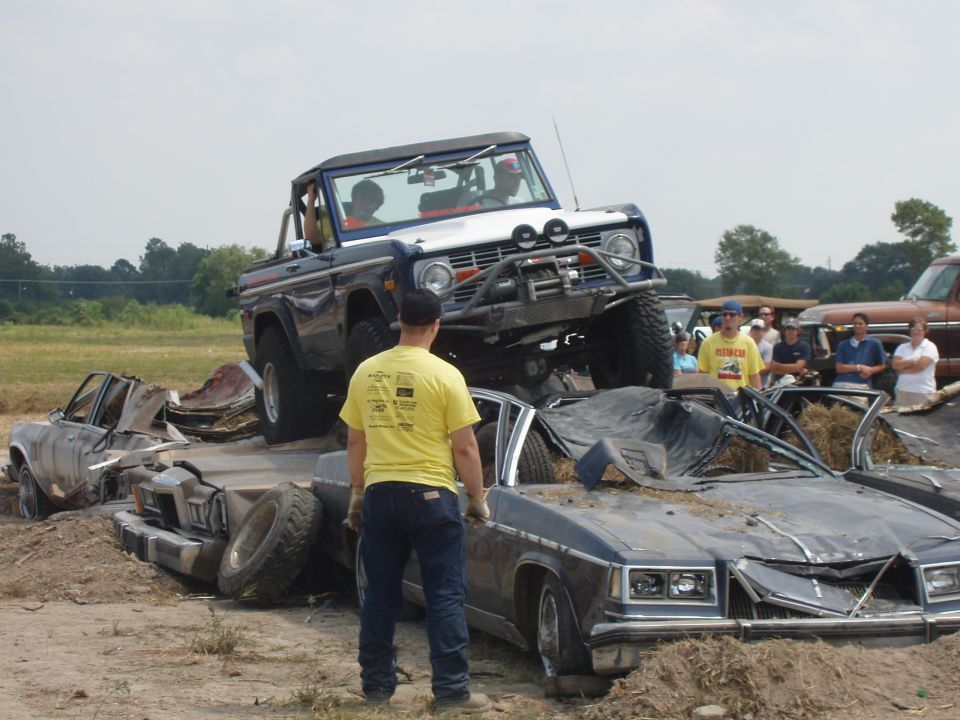 Ford Bronco on top of crushed cars, with people watching