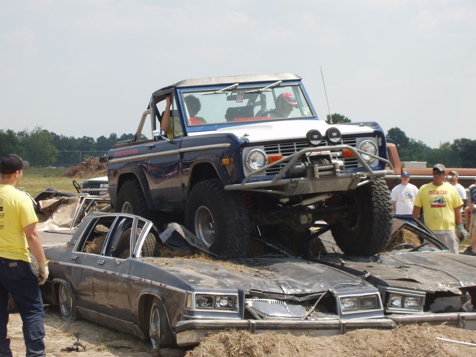Blue Ford Bronco with a winch on a pile of crushed cars