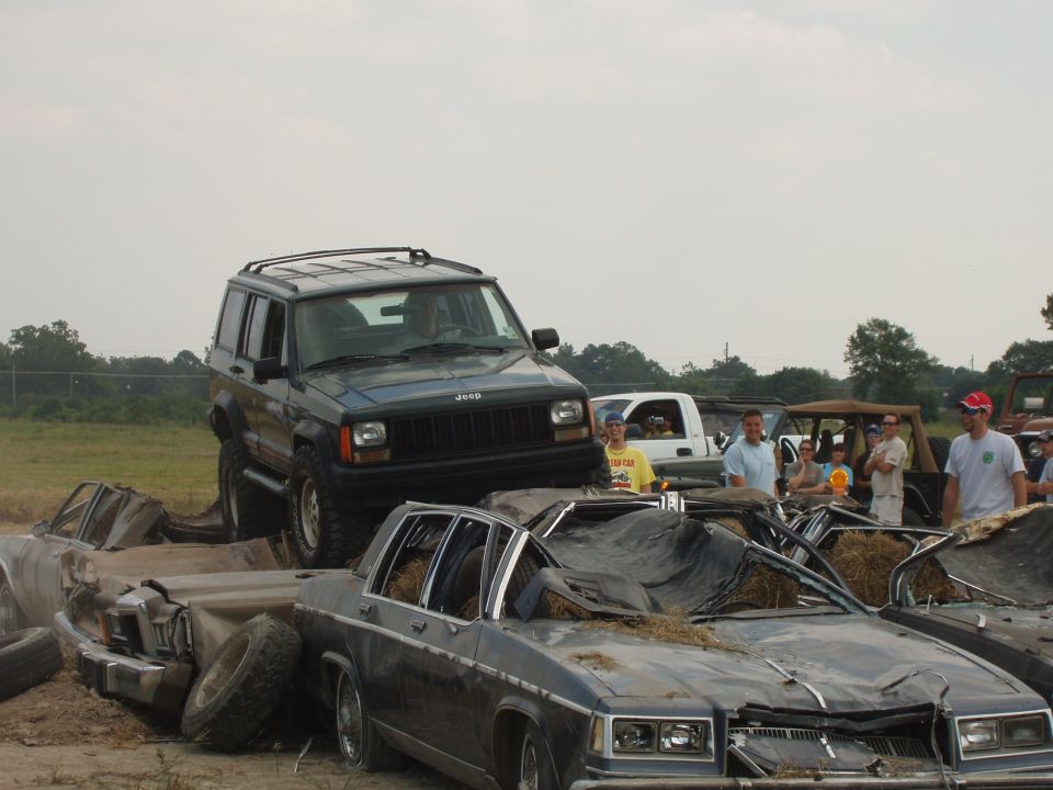 Dark green Jeep Cherokee on crushed cars, front view