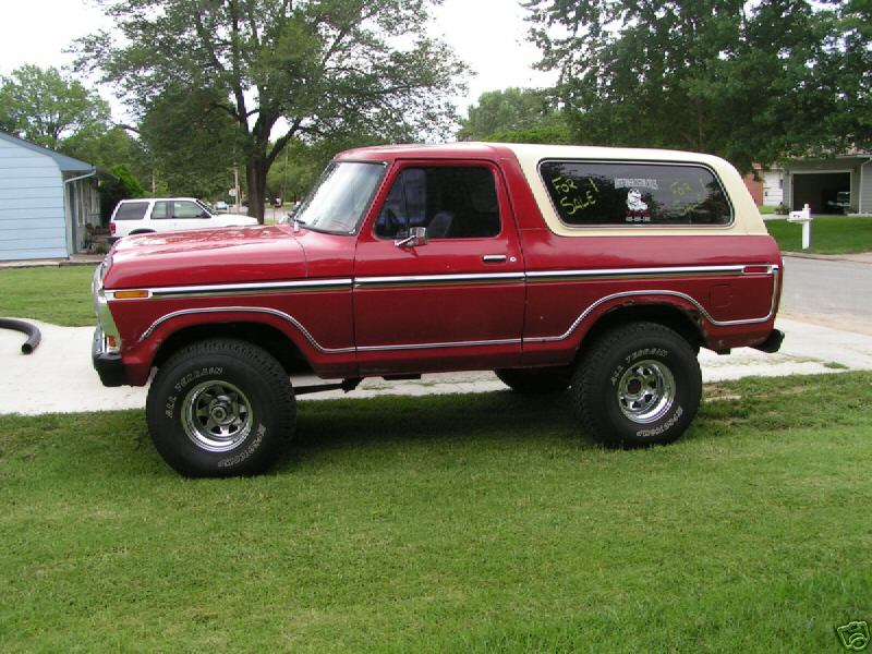 Red and cream 1978 Ford Bronco side view on lifted tires with For Sale signs in rear window, parked on a driveway