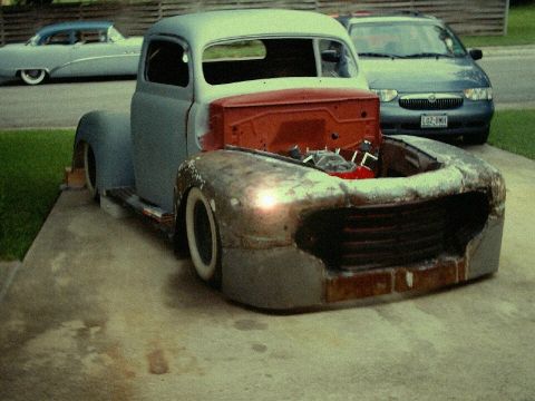 1972 Ford Ranchero - A custom pickup truck in a state of disrepair sits on a concrete driveway next to a blue sedan.