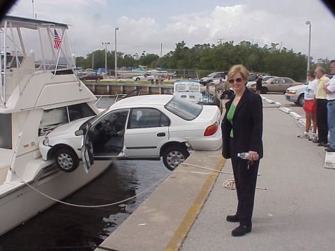 1972 Ford Ranchero - A white sedan is precariously positioned on the side of a yacht at a marina, with its driver's door ajar.