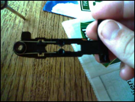 Hand holding a small black plastic mechanism on a wood table, blurry close-up