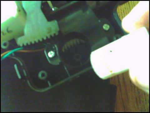 1988 Ford Bronco - A white plastic component is examined against a complex mechanical assembly gears and wiring.