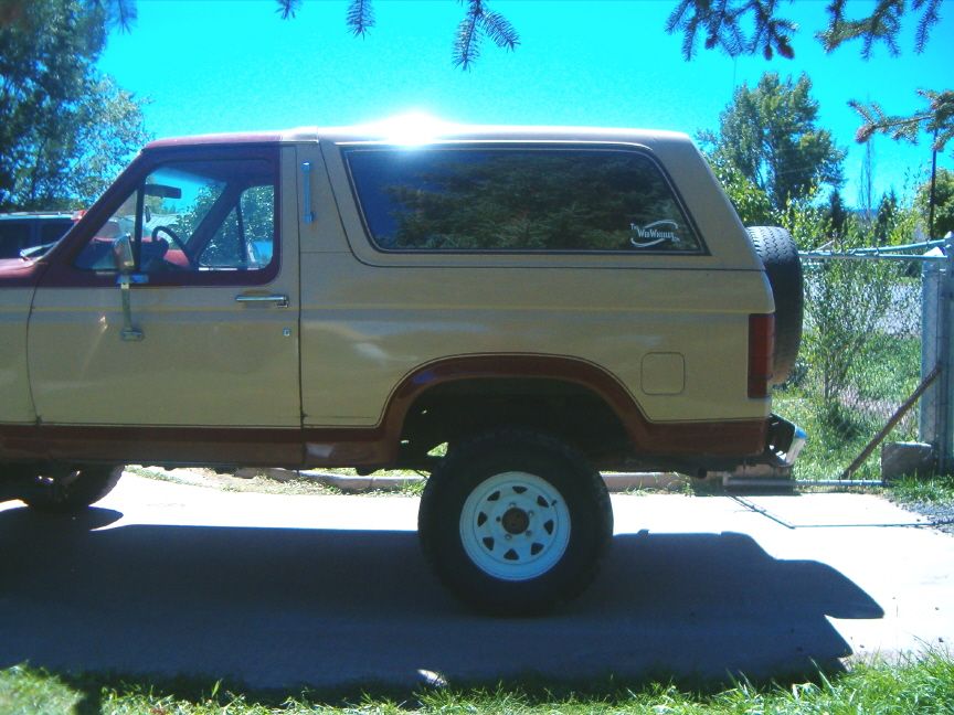Side profile of tan and red two-tone full-size Ford Bronco with white wheels, spare on rear