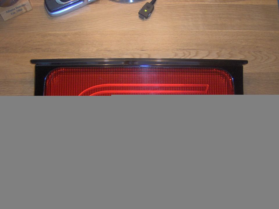 Red car taillight assembly with black trim, lying on a wooden surface