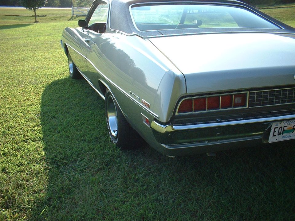 Silver car parked on grass, rear view. Chrome bumper, rectangular taillights, and a black vinyl roof are visible