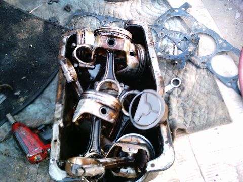 1986 Ford Bronco - A steel oil pan used as a parts bin, filled with used pistons still attached to their connecting rods plus rod caps and hardware, sitting o…