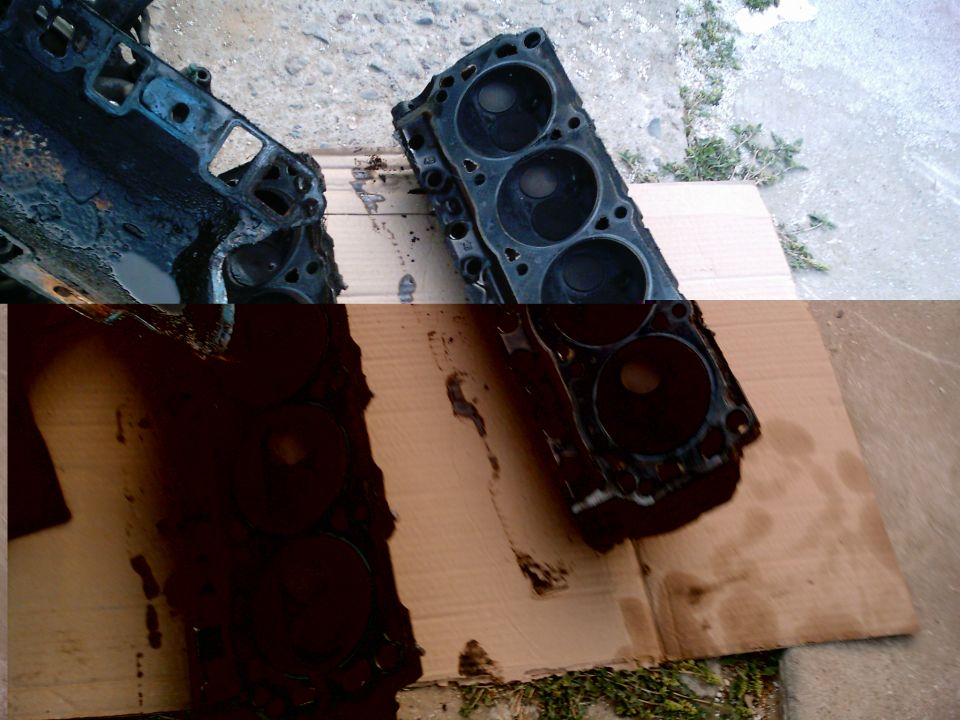 Pair of greasy V8 cylinder heads face-up on cardboard on a driveway