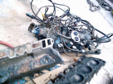 1986 Ford Bronco - Disassembled engine components, including an intake manifold and cylinder head, are laid out on a concrete surface.