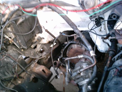 1986 Ford Bronco - A stripped engine bay of a light-colored truck with the engine pulled, showing the radiator, core support, dangling wiring harness and hose…
