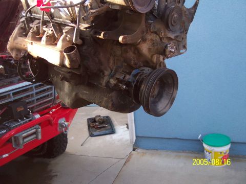 1985 Ford Bronco - An engine assembly is suspended in the air, with the front of a red vehicle visible beneath it.