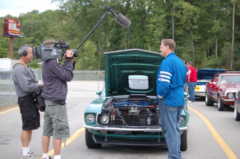 2005 Ford Deluxe - A green 1969 Ford Mustang Mach 1 is filmed with its hood open, parked alongside other vehicles.