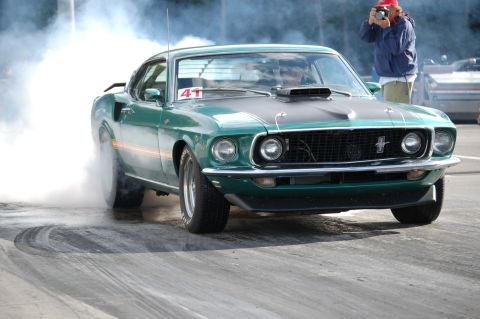 2005 Ford Deluxe - A green 1969 Ford Mustang performs a burnout, emitting a large cloud of smoke. A photographer is visible in the background.