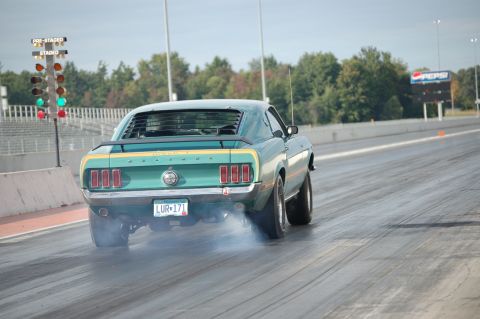 2005 Ford Deluxe - Rear view of a 1969 Ford Mustang Mach 1 performing a burnout at a drag strip.