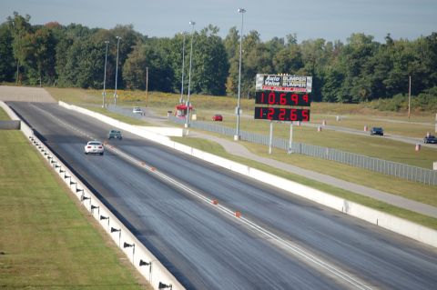 2005 Ford Deluxe - Cars race down a drag strip under a scoreboard displaying elapsed times.