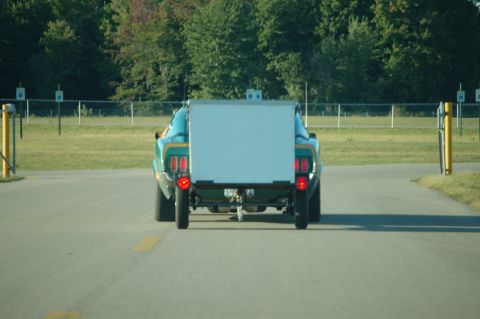 2005 Ford Deluxe - A vintage green coupe tows a white trailer from behind.