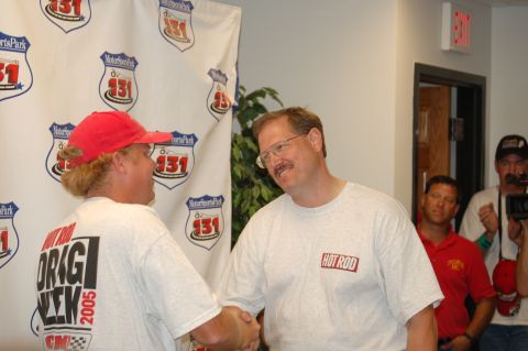 2005 Ford Deluxe - Two men shake hands in front of a "MotorsportsPark 131" banner. One man's shirt displays "HOT ROD DRAG WEEK 2005".