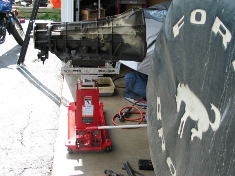 1995 Ford Bronco - A transmission is supported by a jack, with a spare tire cover the Ford Bronco logo visible.