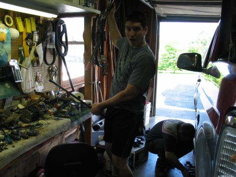 1995 Ford Bronco - Two men are working on a red vehicle inside a cluttered garage.