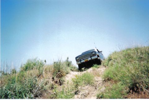 1986 Ford Bronco - Pickup truck navigates a steep, grassy incline under a bright blue sky.