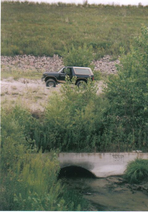 1986 Ford Bronco - A Ford Bronco is seen off-road near a concrete culvert marked with '1938'.