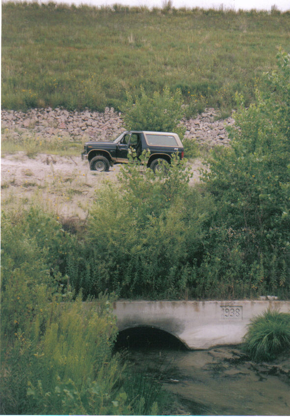 Dark Ford Bronco with white top parked on a creek bank above a 1938 concrete culvert