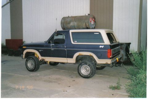 1986 Ford Bronco - A 1986 Ford Bronco is parked outside a building with a large metal tank secured to its roof.