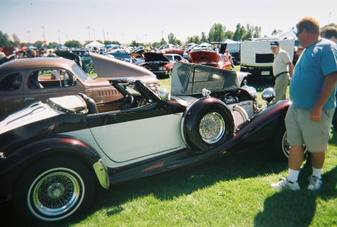 1972 Ford Ranchero - A classic car show features multiple vehicles, including a two-tone convertible with its hood up.