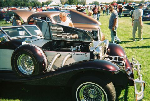 1972 Ford Ranchero - An Excalibur car is displayed with its hood open at an outdoor car show, revealing the engine and distinctive side exhaust pipes.
