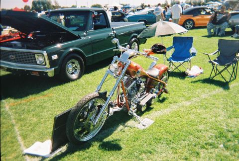 1972 Ford Ranchero - A custom chopper motorcycle is displayed on grass next to a green pickup truck at an outdoor event.