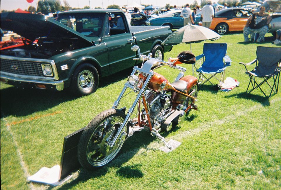 Custom chopper motorcycle with orange flame paint, chrome details, and a green pickup truck in the background