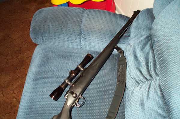 Rifle with scope resting on a blue couch