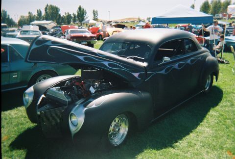 1972 Ford Ranchero - A black hot rod coupe with flame decals is displayed at an outdoor car show.