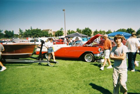 1972 Ford Ranchero - A classic red and white convertible is displayed at an outdoor event with attendees and a boat on a trailer.