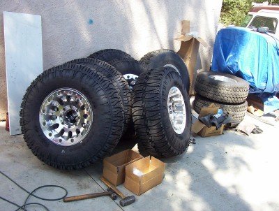 1995 Ford Bronco - A collection of tires and rims are visible in front of a tarp-covered vehicle.