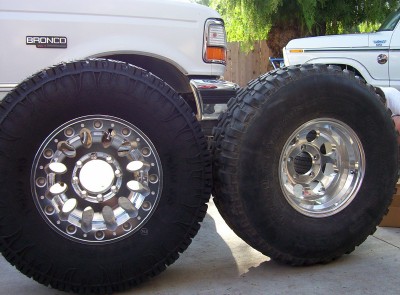 1995 Ford Bronco - Two large off-road tires and wheels are shown in front of two Ford trucks.