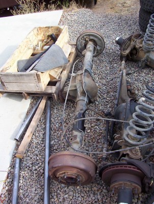 1995 Ford Bronco - Various vehicle axle and suspension components are displayed outdoors on a gravel surface.