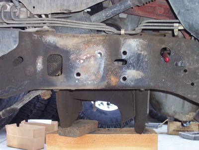 1995 Ford Bronco - The underside of a vehicle shows a heavily rusted frame with various suspension components and brake lines.