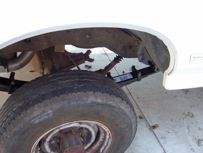1995 Ford Bronco - Close-up view of the rear suspension and tire of a white vehicle, showing leaf springs and exhaust pipe.